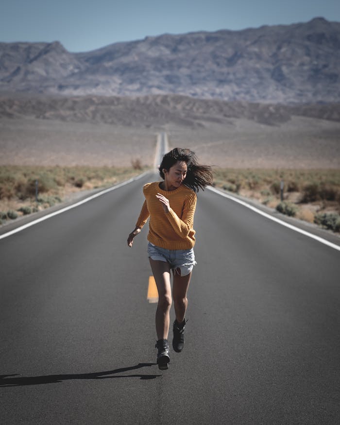 Services-01 An Asian woman runs confidently on a long, remote desert highway under clear blue skies.