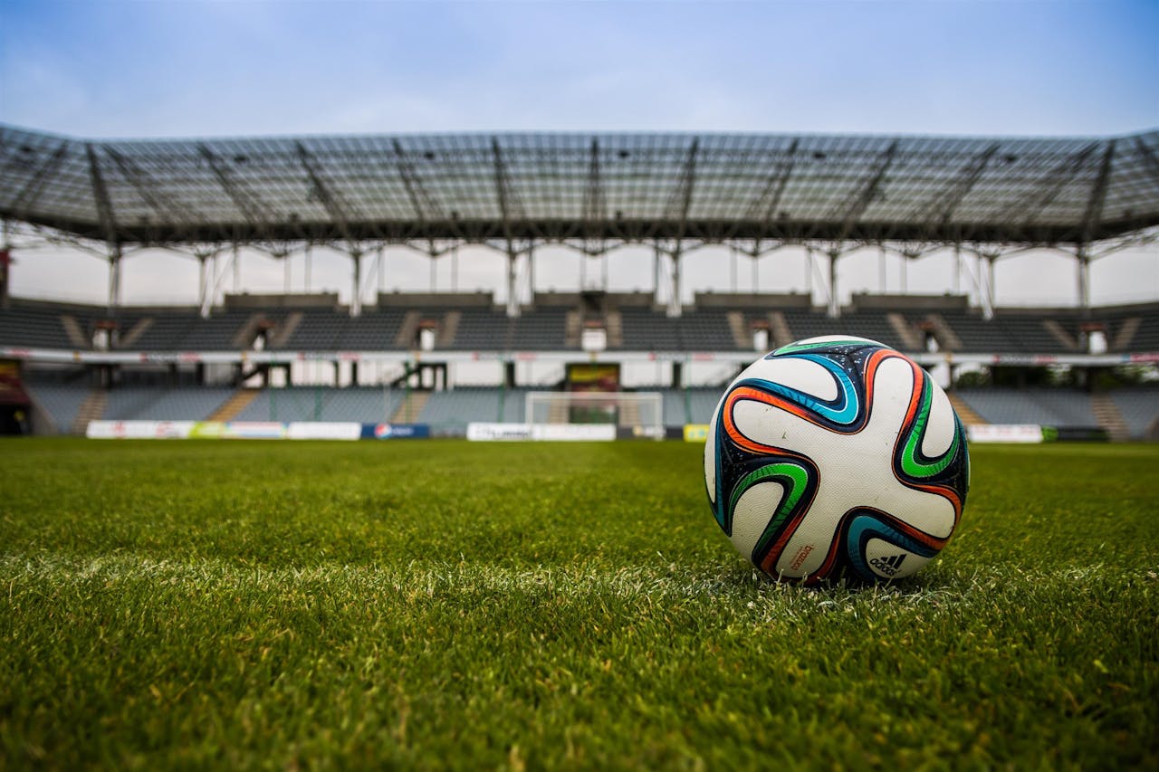 Services-03 Close-up of a soccer ball on a lush grass field with an empty stadium in the background.